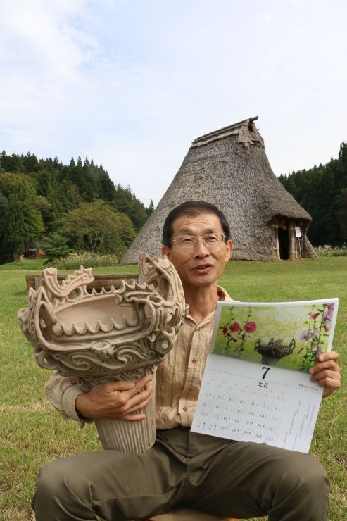 火焔型土器のレプリカとカレンダーを手に、笹山遺跡をＰＲする野沢恒雄さん＝十日町市