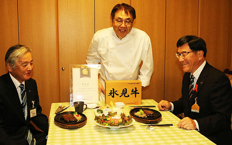 谷内代表（中央）から氷見牛のステーキなどの説明を受け、笑顔を見せる林市長（右）と伊藤組合長