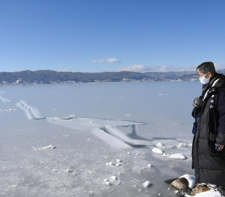 全面結氷した湖面にできた幅３０センチほどの割れ目を確認する宮坂宮司＝１３日午前１０時５６分、諏訪市