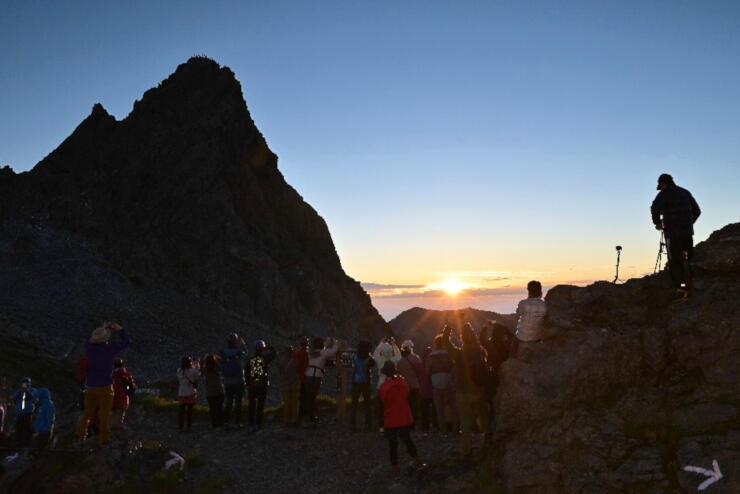 北アルプス槍ケ岳越しに御来光を眺める登山者ら＝２３日午前４時５１分、槍ケ岳山荘近く