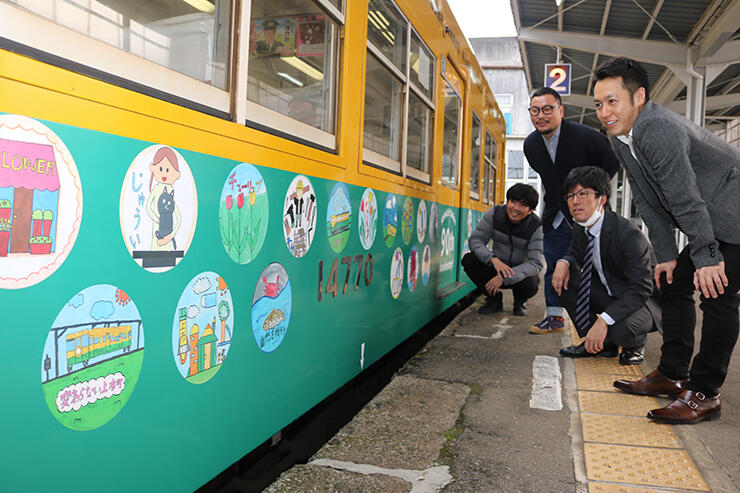 電車を彩る児童の絵を眺める伊東部長（左から２人目）ら青年部員
