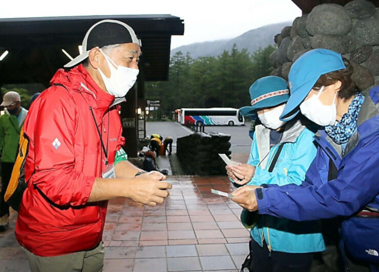 寄付金を集める実証実験について登山客に説明するガイド（左）＝９月１８日、上高地インフォメーションセンター前