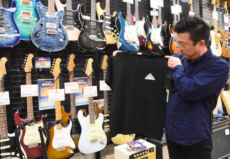 島村楽器松本パルコ店で取り扱う「信州ギター」の前で記念ＴシャツをＰＲする太田さん