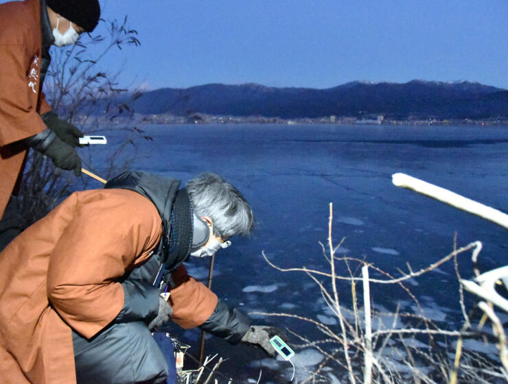 諏訪湖のほとりで氷を割って水温を計る宮坂宮司（手前）ら＝７日午前６時３７分、諏訪市豊田