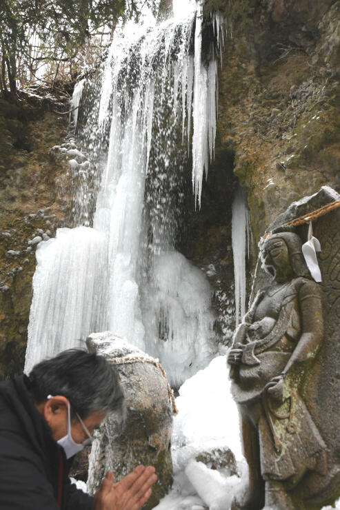 氷柱ができている「不動の滝」と、傍らの石像に手を合わせる花岡さん＝２０日午前９時１０分