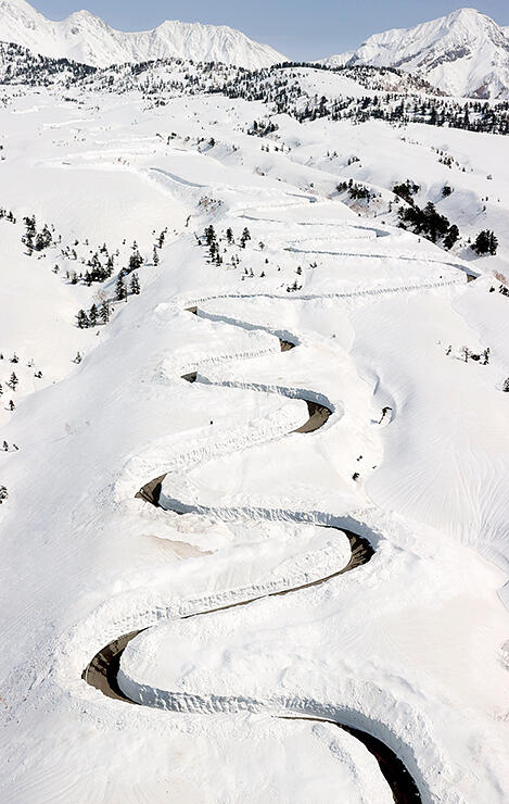 雪原に除雪の跡が曲線を描く七曲周辺の高原バス道路＝１６日午後１時２５分ごろ（本社チャーターヘリから）