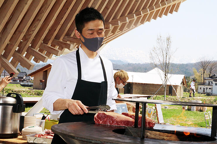 立山連峰をバックに特製の鉄板で熟成肉を焼く柳瀬さん
