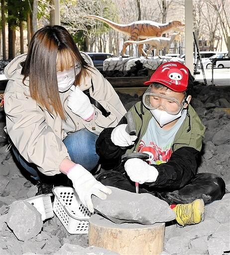再開したホロッサで化石を発掘する親子。奥はこの日お目見えした恐竜モニュメント＝４月１７日、福井県大野市角野