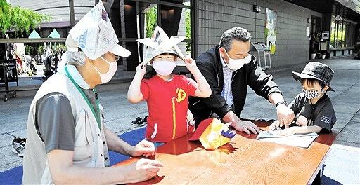 サポーターズクラブのメンバーに教えてもらって新聞紙でかぶとを折る子どもたち＝５月７日、福井県福井市の県立歴史博物館