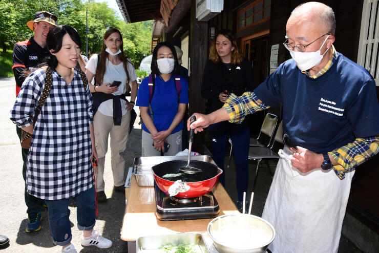 収穫した山菜を天ぷらにする様子を見る参加者ら