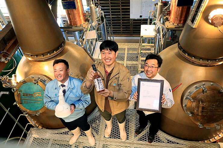 ＺＥＭＯＮで蒸留し初めて商品化したウイスキーを手にする稲垣さん（中央）と老子さん（左）、氷見さん。左右にあるのがＺＥＭＯＮ