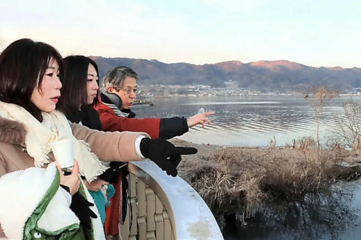 宮坂宮司（左から３人目）と諏訪湖を眺める観光客たち＝２２日午前７時７分、諏訪市豊田