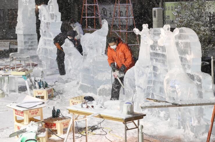 厳しい冷え込みの中、氷の彫刻を制作する作家ら＝２７日午後８時３１分、松本市の松本城大手門枡形跡広場