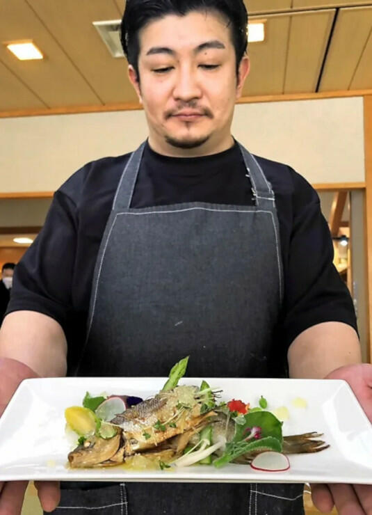 佐久市産シナノユキマスや南相木村産の野菜を使った料理を手にする鈴木さん