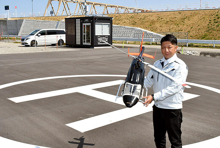 ヘリパッドトナミで、ヘリの模型を持つ石村さん