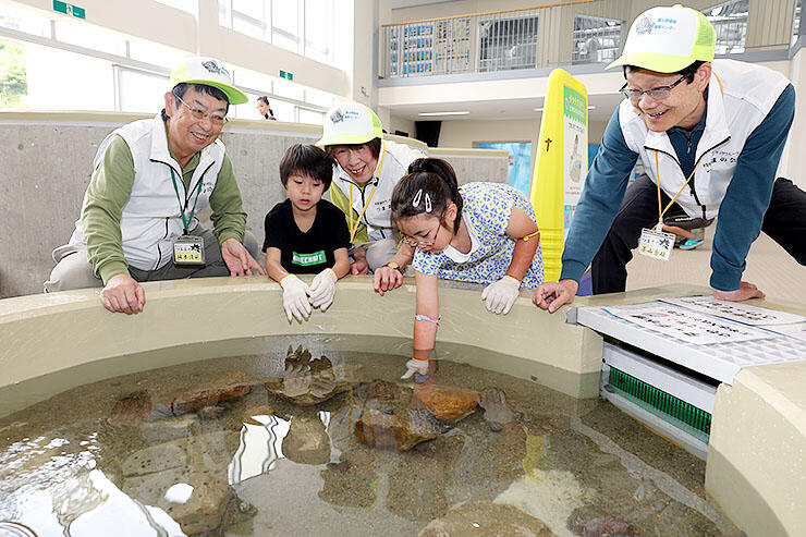 富山湾の生き物と触れ合えるコーナーで子どもたちと話す茶山会長（右）らメンバー