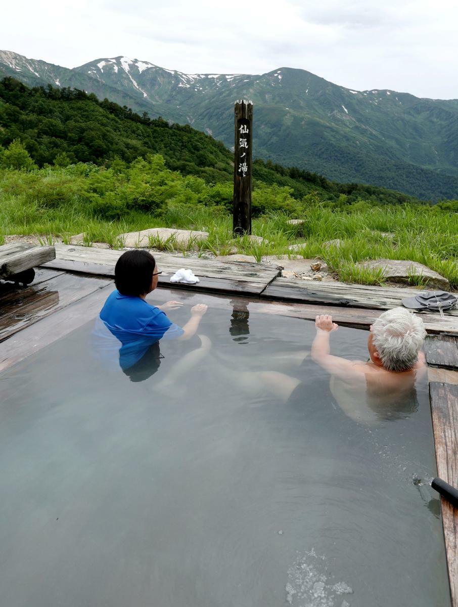 雪が残る山並みを眺めながら湯を楽しんだ観光客＝７月５日、糸魚川市の蓮華温泉