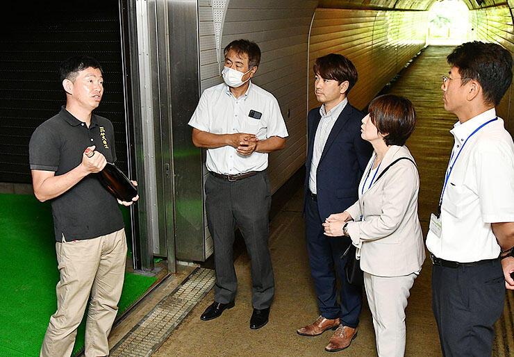 菅沼合掌造り集落にあるトンネルでの日本酒熟成について、ＪＡ職員らに説明する山崎社長（左）