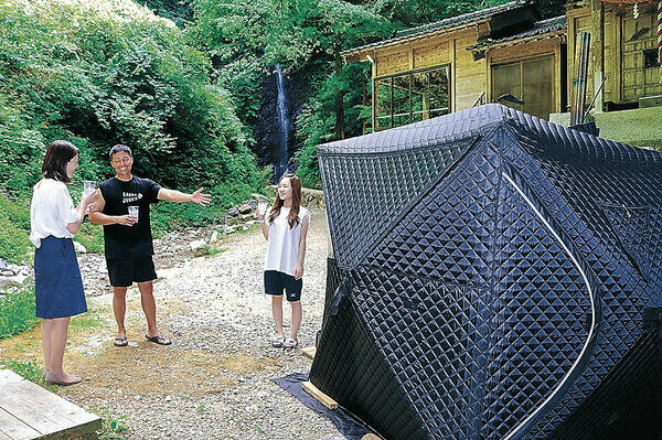 テント型のサウナに入った後、外気浴を楽しむ関係者。奥には不動滝が流れる＝中能登町井田の不動滝