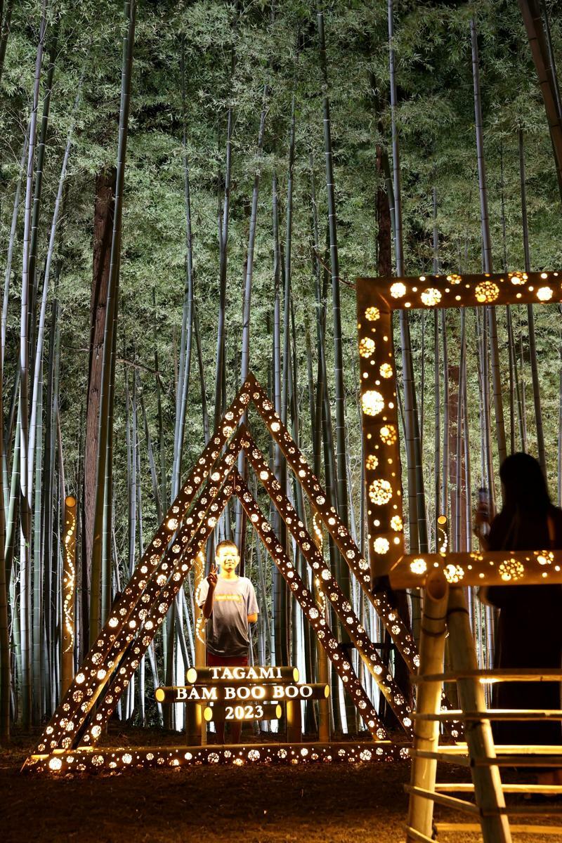 竹林の会場には竹あかりをフレーム状に組んだ撮影スポットを多数設けた。光に照らされた竹林をバックに、来場者は写真に収まっていた＝田上町吉田新田